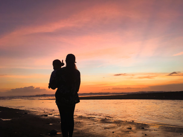 母亲和孩子在沙滩上的剪影照片与日落的背景图片下载
