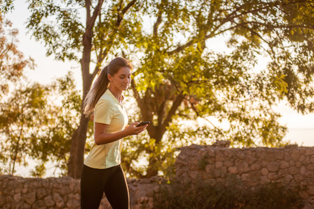 穿着运动服的年轻女子的特写照片，在海边的公园里慢跑，手里拿着智能手机图片下载