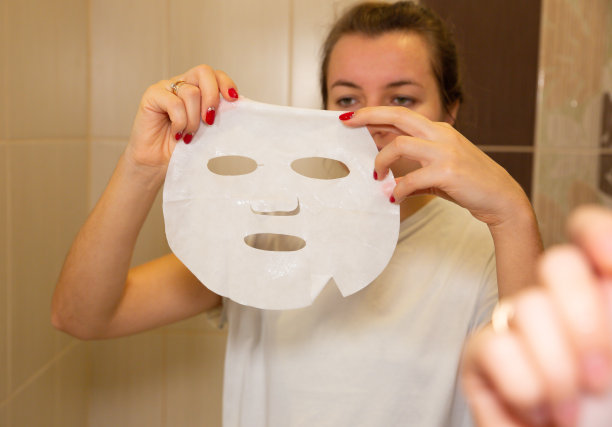 女孩手里拿着面膜片。在家做美容面部手术。图片下载