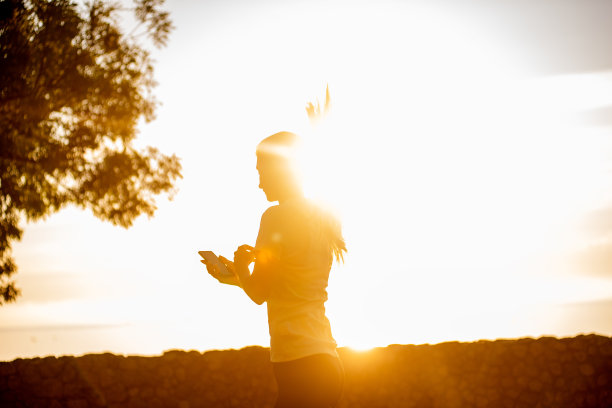 穿着运动服的年轻女子的特写照片，在海边的公园里慢跑，手里拿着智能手机图片下载