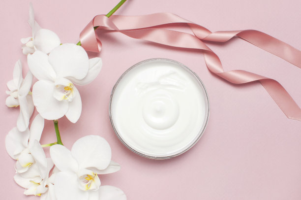 美容水疗概念。打开的塑料容器与奶油和白色蝴蝶兰兰花在粉红色的背景平铺俯视图。草药皮肤科化妆品卫生霜，有机化妆品天然图片下载
