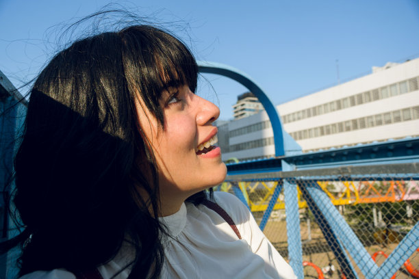 年轻的拉丁大学女孩站在桥上，微笑着抬头看。图片下载