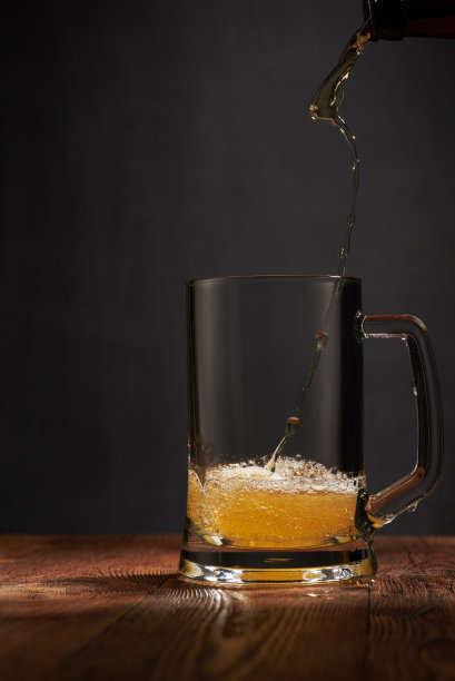 泡沫和琥珀色的精酿啤酒，从瓶中倒入木条上的马克杯。黑暗的背景。使用copyspace的浅景深照片。图片下载