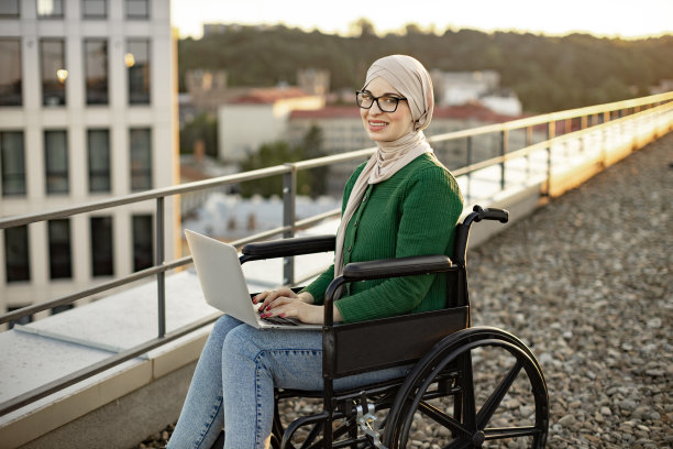 坐在轮椅上拿着笔记本电脑的商务女士在阳台上摆姿势图片下载