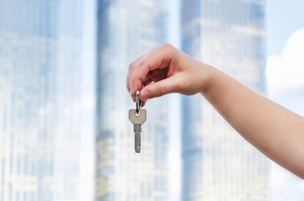 在新建筑的模糊背景中，女性手握钥匙。拿着钥匙靠近点图片下载