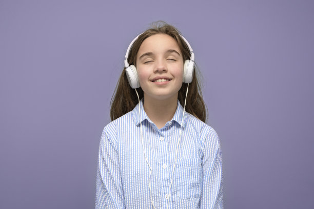 十几岁的女孩戴着耳机享受音乐。粉红色的背景图片下载