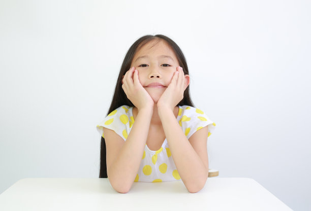 漂亮的亚洲小女孩把下巴放在桌子上的手在白色的背景图片下载