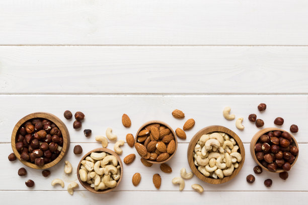 五颜六色的桌子上，木碗里有各式各样的坚果。腰果，榛子，核桃，杏仁。顶部视图与复制空间的混合图片下载