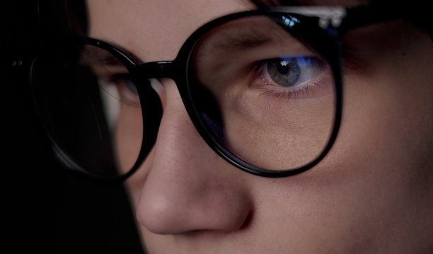 一个戴着眼镜的人正在从黑暗中看光。男性使用电脑屏幕，互联网，电视，智能手机。看书、看电视、上网工作到很晚。图片下载