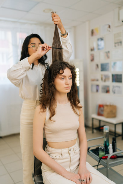 现代美容工作室里，女发型师在用夹子卷发后用梳子梳理漂亮年轻女客户的长发。图片下载