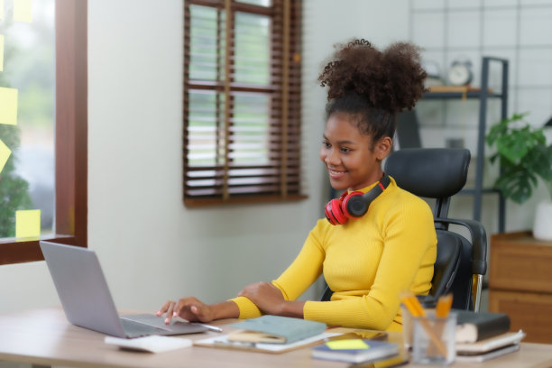 年轻漂亮的黑人女性在家用笔记本电脑工作。年轻的卷发非裔美国女性在家里用笔记本电脑做笔记。图片下载