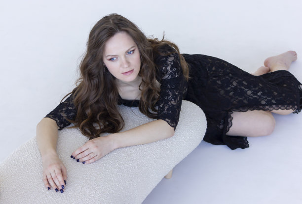 年轻的白人女子倚在白色背景的米色躺椅上。一头棕色长发的美丽白人女性把目光移开。现代舒适家具。水平面。图片下载