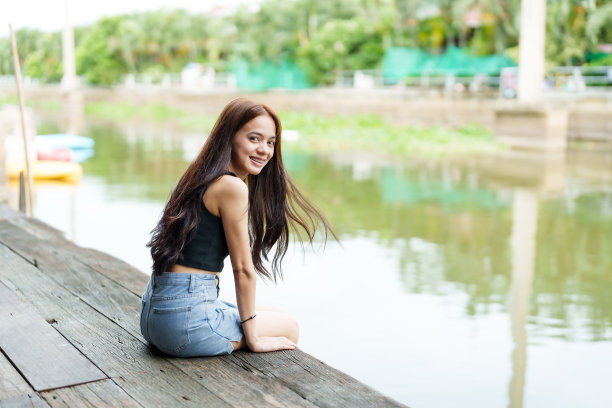 可爱的亚洲女孩长发穿着短袖坐在水里，在码头的空闲时间放松。周末带着笑脸在河边，乡村的运河，清澈的水图片下载