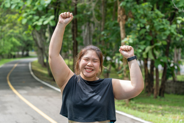 在当地公园的跑道上成功地完成了晨跑后，一位年轻的超重女子微笑着举起双手图片下载