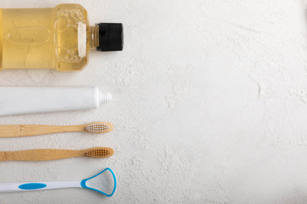 生态竹牙刷，舌清洁剂，牙线，牙齿模型，牙膏管和漱口水在灰色背景与复制空间。平的。口腔卫生。口腔护理产品套装。牙医的概念图片下载