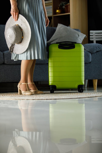 一个女人拿着太阳帽，站在她收拾好的手提箱旁边图片下载