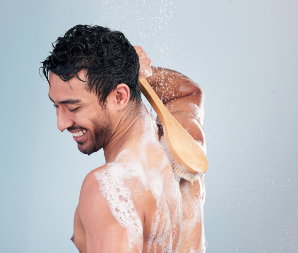 特写：面带微笑的男子在蓝色背景的淋浴中用刷子刷背图片下载