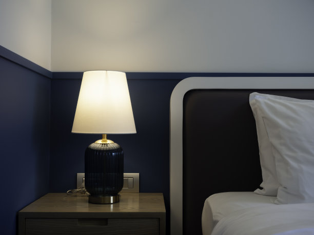 豪华台灯，白色面料，蓝色玻璃，金色材质，在卧室附近的深蓝色墙壁背景上闪闪发光。在黑暗中点灯。图片下载