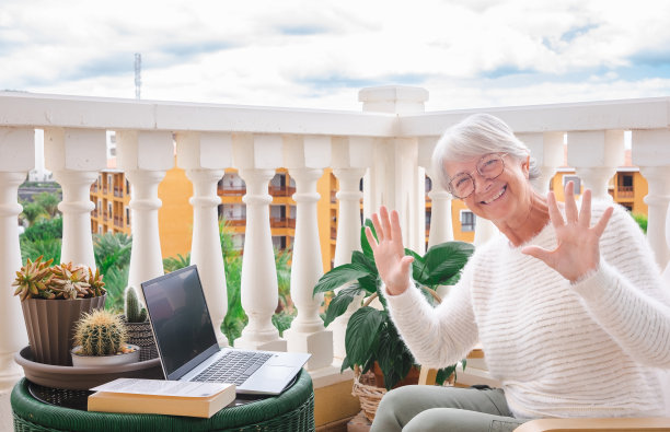 乐趣和愉快的年长妇女坐在家里阳台后远程工作看着相机-成年人有吸引力的女性享受安静的生活方式户外挥手图片下载