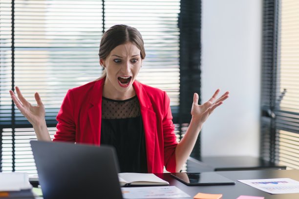 一个压力大、沮丧的女商人坐在办公桌前，因为业务上的错误或危机而愤怒地对着笔记本电脑大喊大叫。图片下载