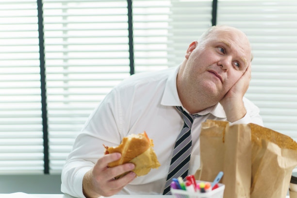 胖子在办公室吃垃圾食品。图片下载