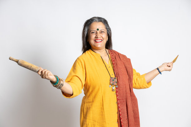 幸福成熟的印度老年妇女的肖像拿着擀面杖和木勺孤立在白色背景。家用电器，厨房概念。图片下载