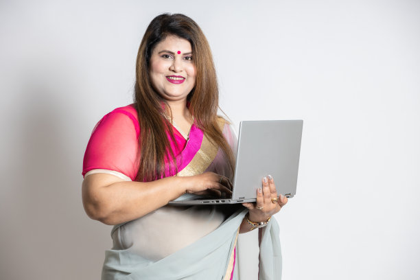 幸福自信的印度城市女性穿着纱丽，站在白色背景上摆弄笔记本电脑。图片下载