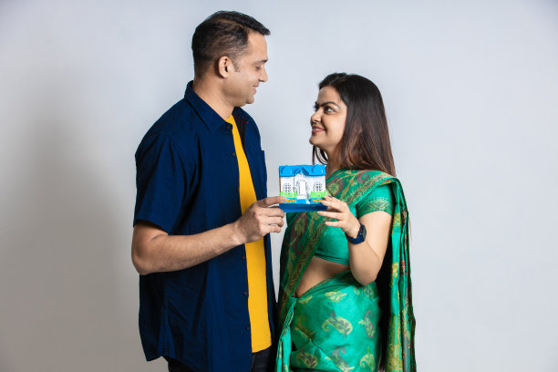 快乐的年轻印度夫妇手里拿着一个玩具房子，孤立在白色背景上，新公寓，住房贷款，租赁财产和房地产概念，复制空间。图片下载