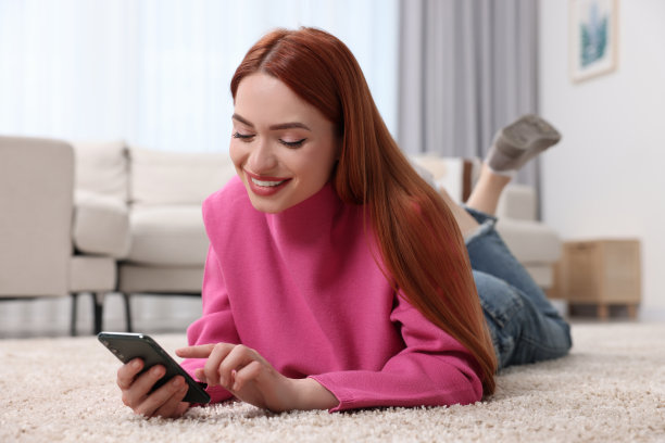 快乐的女人在家里的地板上用智能手机发短信图片下载