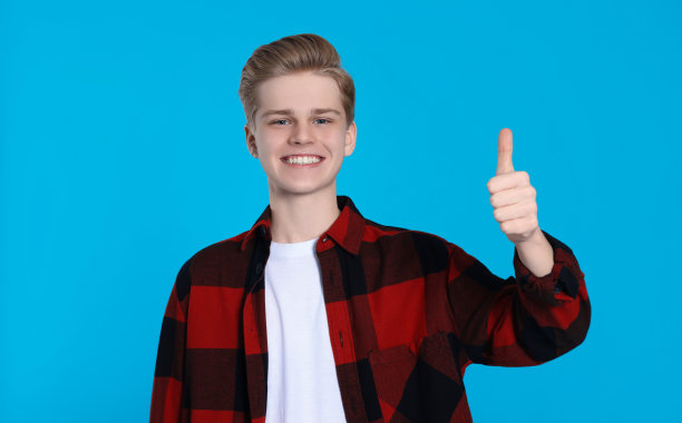一个十几岁的男孩在浅蓝色背景上竖起大拇指图片下载