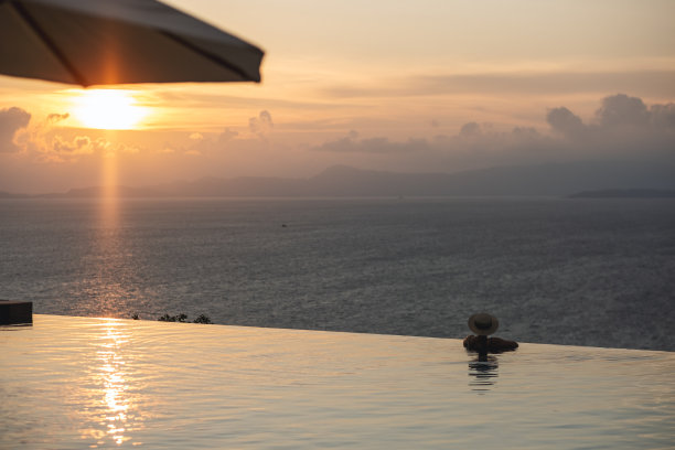 后视图形象的一个女人与帽子放松在无限游泳池，看着美丽的日落和海景图片下载