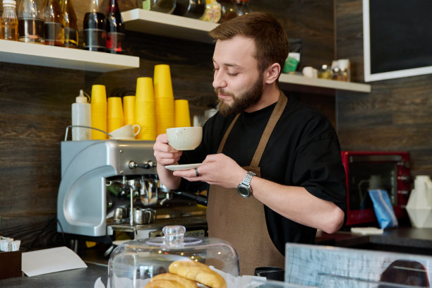 男咖啡师的肖像，系着围裙，端着刚煮好的卡布奇诺咖啡图片下载