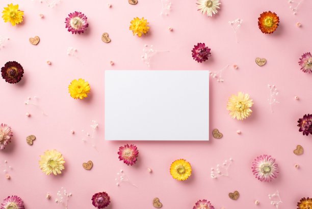 俯视照片的白色明信片和许多不同的可爱的花与小木屑的心形字母散落在柔和的粉红色背景图片下载