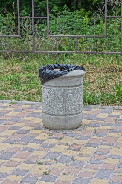 一个灰色的混凝土瓮和一个黑色的袋子矗立在棕色的人行道上图片下载