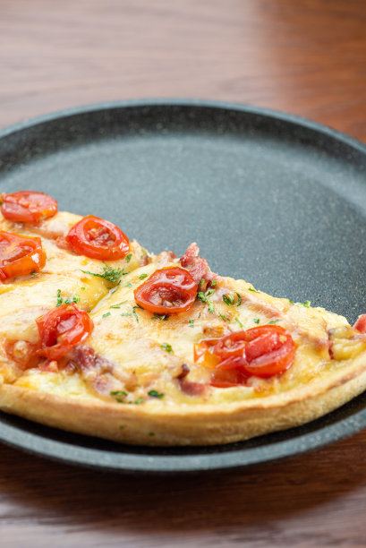 木桌上的披萨。半个披萨放在黑煎锅里。图片下载