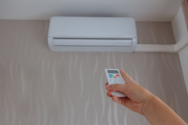女人的手握着空调的遥控器，调节着房间的温度图片下载