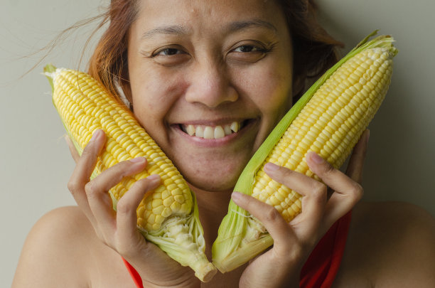 一个亚洲女人拿着玉米面带微笑图片下载