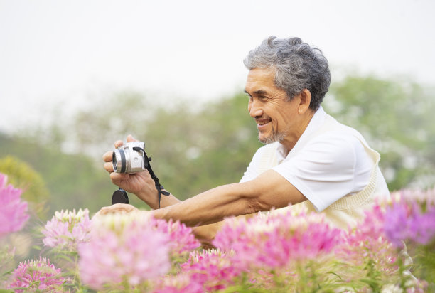 一位亚洲老人喜欢在夏日花园中拍摄粉红色的花朵图片下载