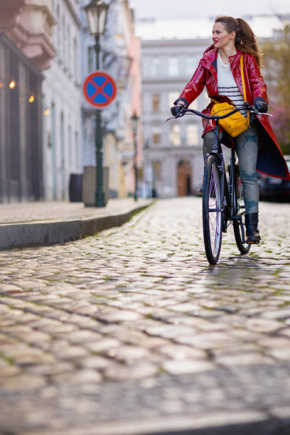 身穿红色雨衣的女子在城市街道上骑自行车图片下载