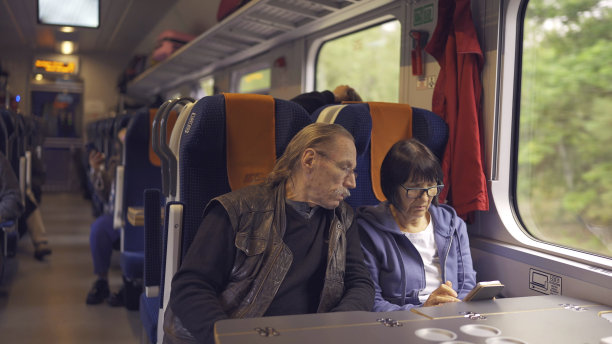 老夫妇乘火车旅行，女士手里拿着手机，两人都在看智能手机，互相交谈图片下载
