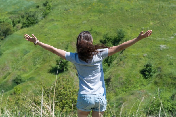 快乐的女人在绿草如茵的峡谷里迎接太阳。年轻的女性向阳光举手。图片下载