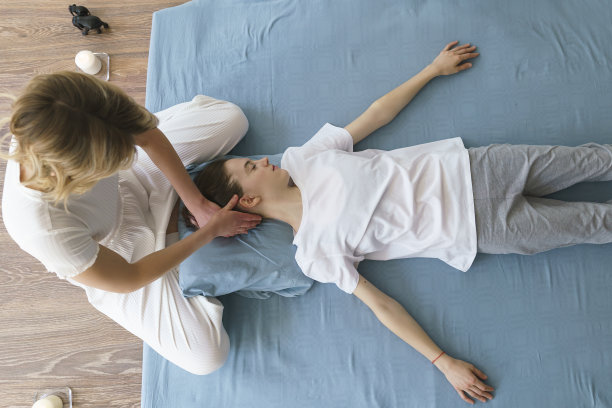 年轻的女按摩师在地板上做泰式按摩，按摩她的脖子和肩膀图片下载