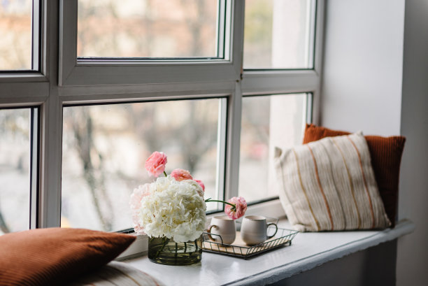 白色的窗台上放着鲜花，咖啡杯，舒适的枕头，装饰的空间。家庭房间、房屋内部设计。现代装饰的室内场所。舒适的公寓。春天静物场景。图片下载
