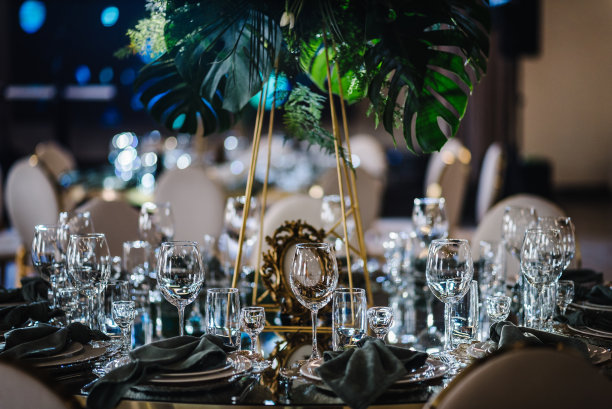 宴会厅装饰组成花卉绿色植物。豪华婚宴。摆好桌子，摆好餐具。生日派对的时髦装饰。客人用的圆桌，盘子，杯子，绿色餐巾。图片下载