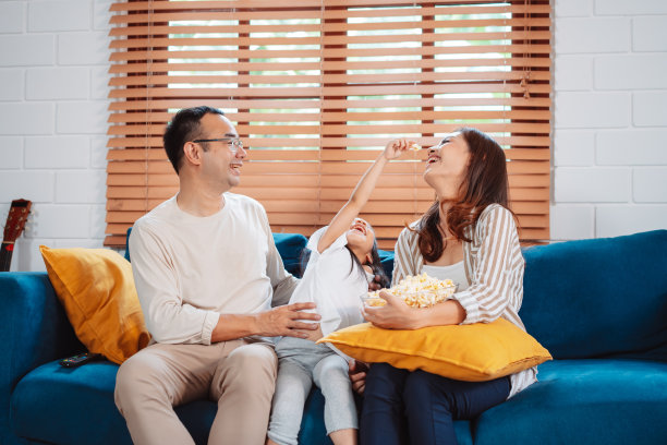 亚洲家庭由父母和女儿在家里客厅的沙发上看电视或电影，吃爆米花组成。享受放松的快乐。图片下载