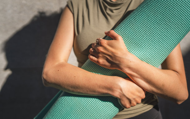 一名白人妇女在阳光明媚的日子里站在户外，手里拿着瑜伽垫图片下载