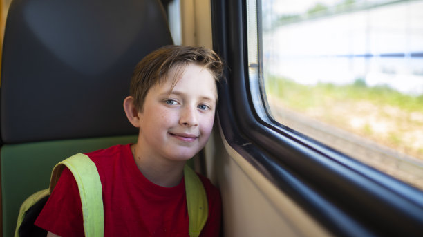 夏天，一个微笑的10岁男孩坐在通勤电车的窗边图片下载