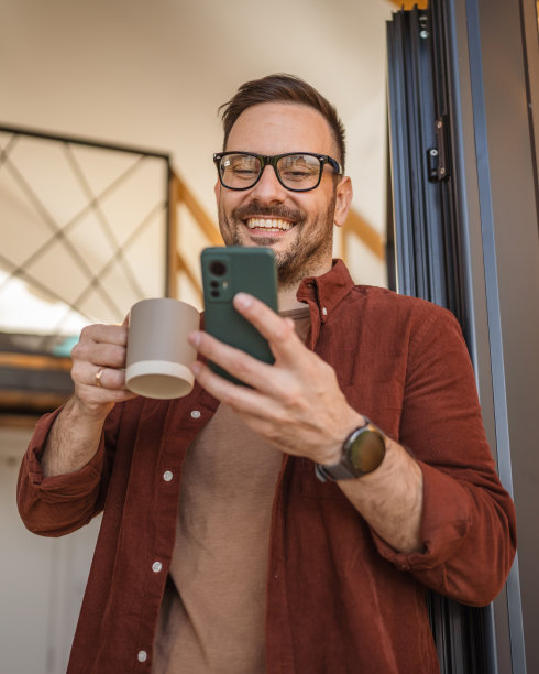 男人站在阳台上用智能手机发短信或短信快乐微笑图片下载