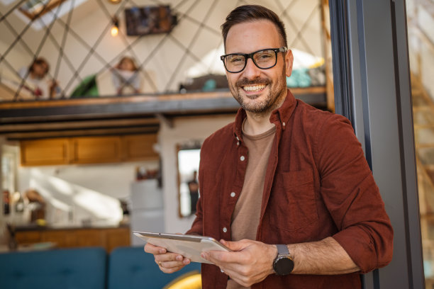 一个白人男子站在阳台上拿着数码平板电脑，开心地笑了图片下载