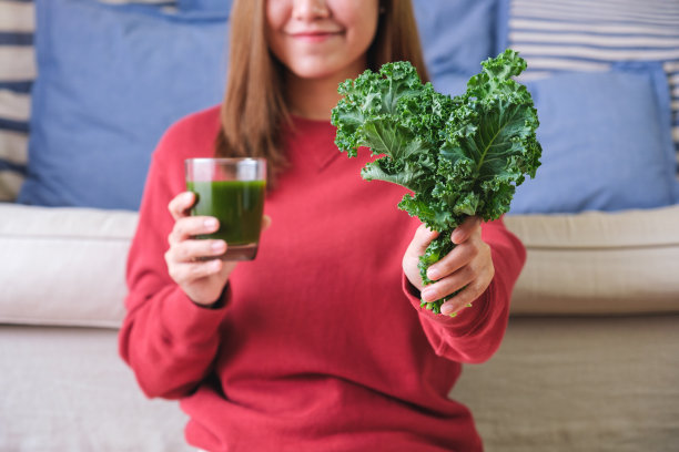一个年轻女子拿着羽衣甘蓝叶子和羽衣甘蓝冰沙的特写照片图片下载